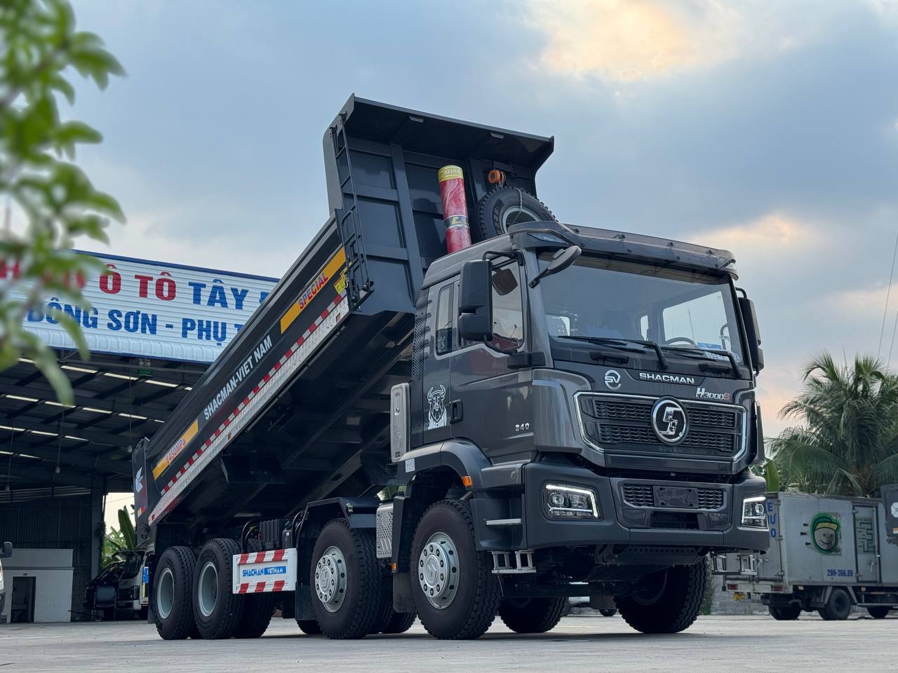 Ảnh chụp góc nghiêng của xe ben Shacman H3000S 8x4 màu xám đậm với thùng xe đang được nâng lên một phần