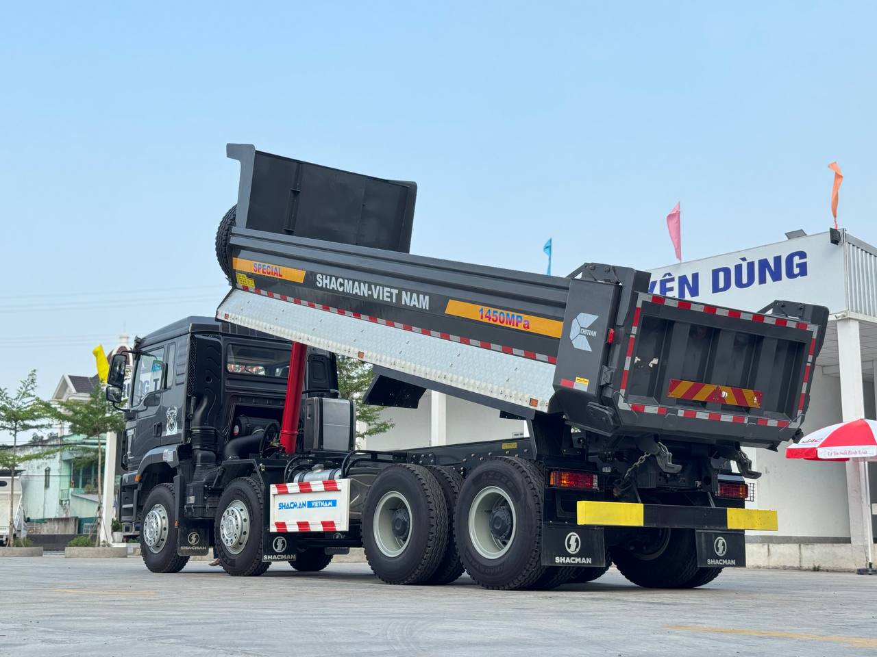 Ảnh chụp góc nghiêng phía sau của xe ben Shacman H3000S 8x4 màu xám đậm với thùng xe được nâng cao hoàn toàn