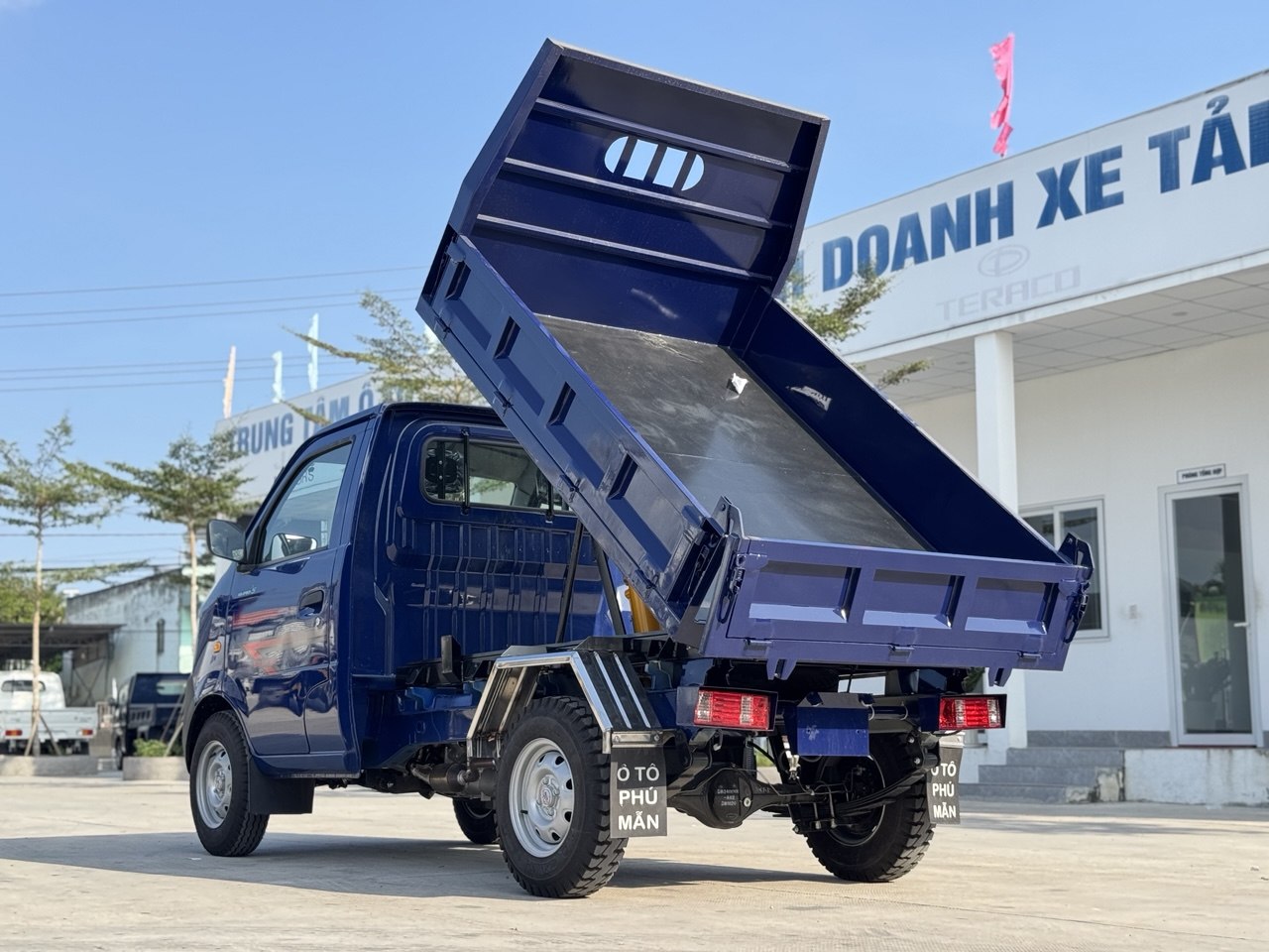 Ảnh chụp góc sau bên trái của xe ben SRM K990 màu xanh dương, thùng ben đang nâng lên