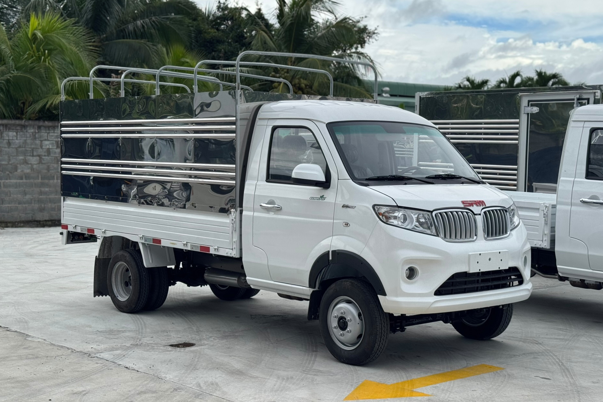 Bối cảnh tại một trạm xăng PVOIL, hai người phụ nữ đang đứng gần trụ bơm xăng. Một phụ nữ mặc áo trắng đội mũ bảo hiểm đen đang xem điện thoại bên cạnh một chiếc xe máy tay ga màu trắng. Một nhân viên PVOIL mặc đồng phục màu xanh đang đứng gần trụ bơm, có thể đang hỗ trợ khách hàng khác. Trụ bơm xăng hiển thị 