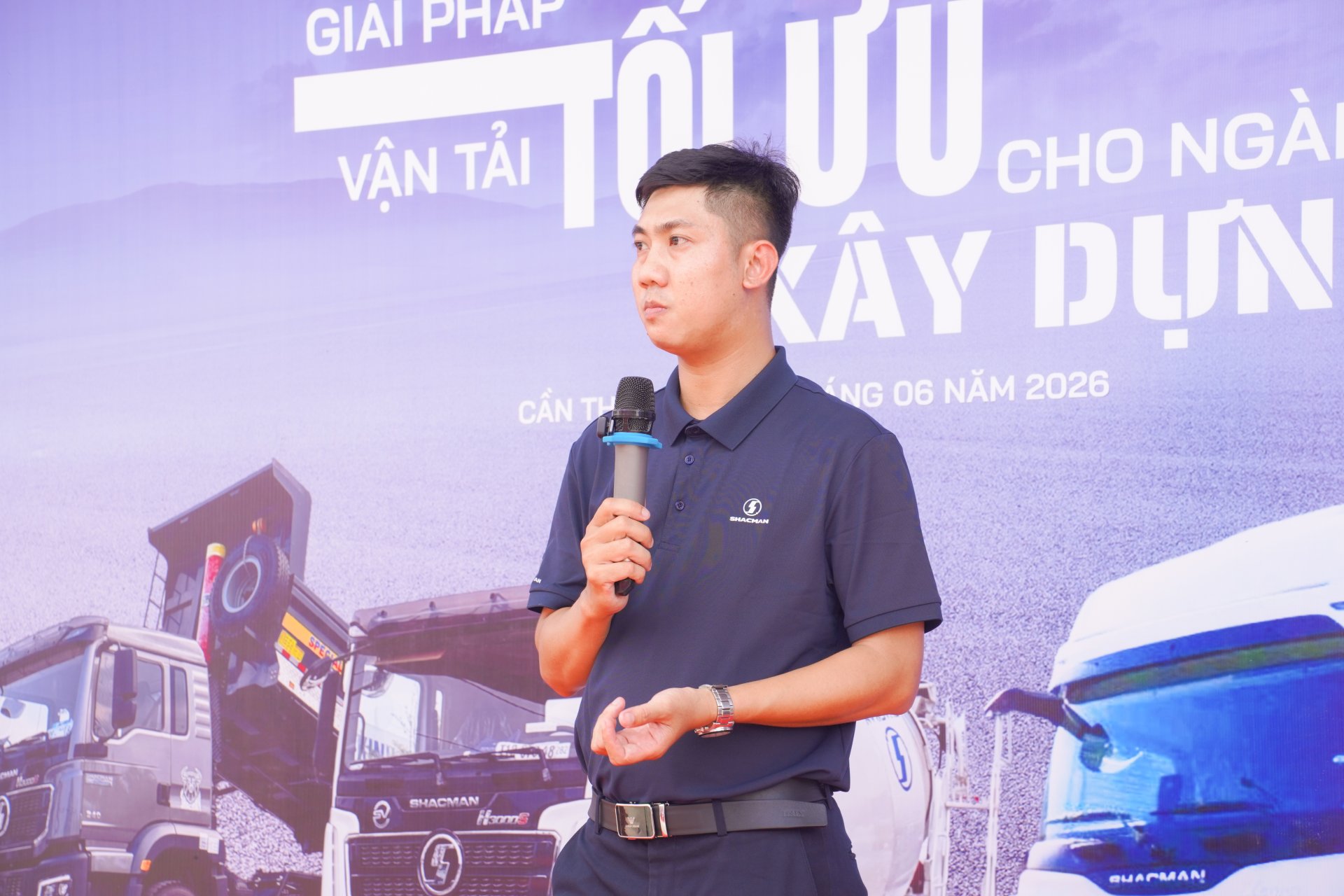 MC/đại diện phát biểu tại sự kiện Shacman với backdrop Giải pháp vận tải tối ưu cho ngành xây dựng