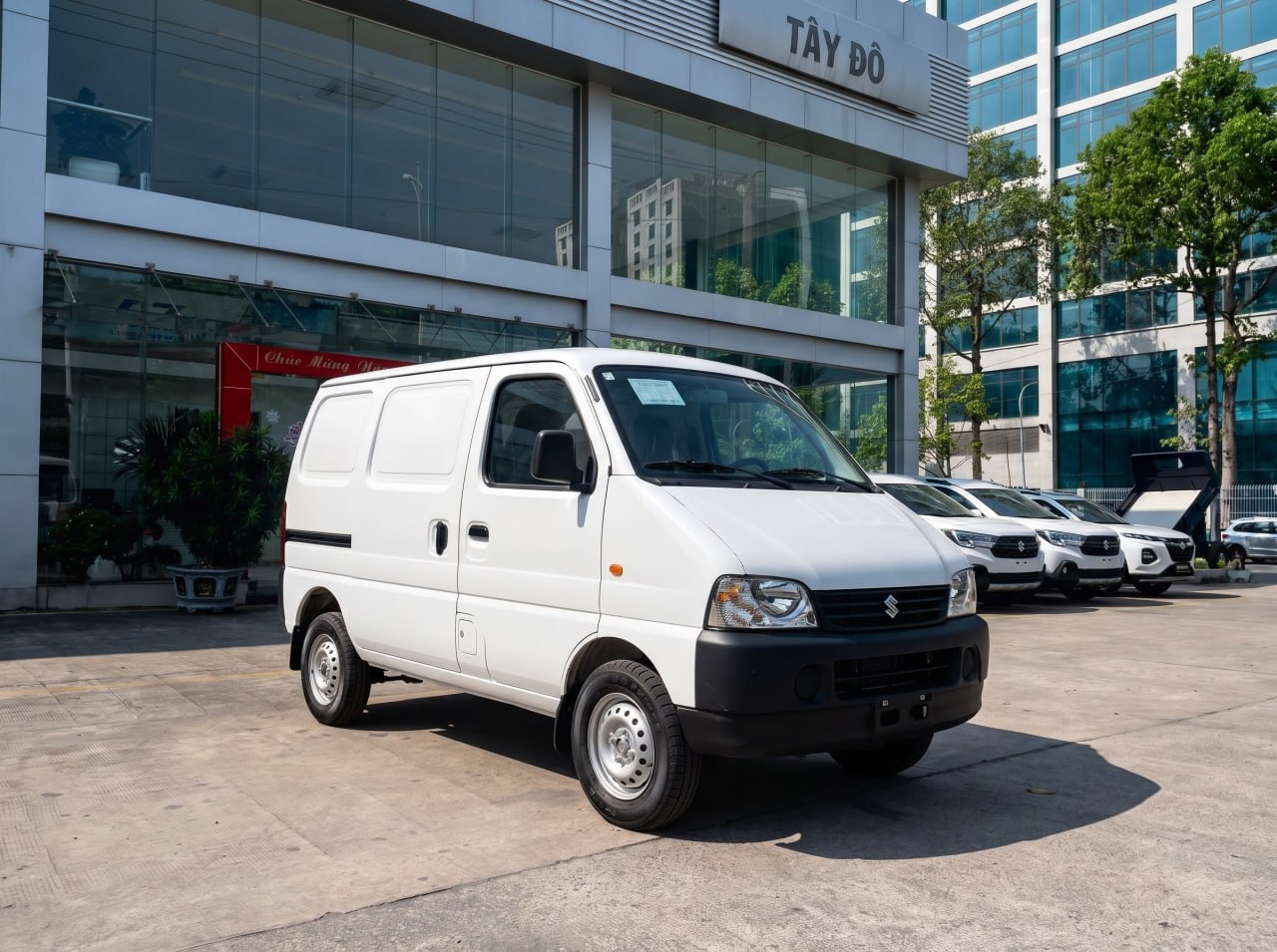 Ảnh ngoại thất xe tải van Suzuki Eeco màu trắng, góc chụp xéo từ phía trước bên trái (3/4 trước), đỗ trước showroom Tây Đô.