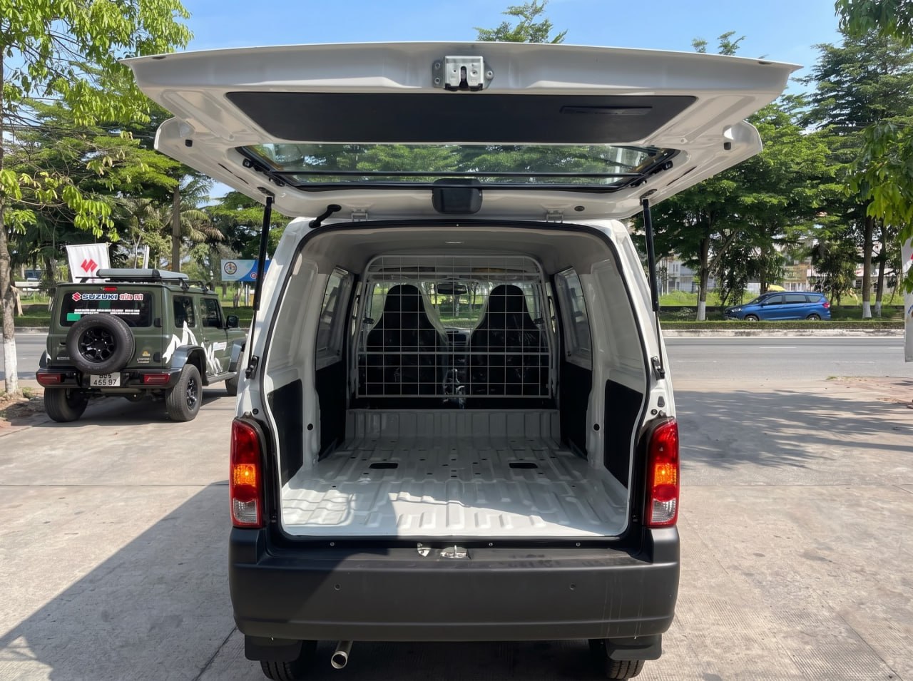 Ảnh ngoại thất và nội thất xe Suzuki Eeco màu trắng, góc chụp từ phía sau khi mở cửa cốp sau, lộ rõ khoang chở hàng trống trải có khung lưới ngăn cách với cabin.