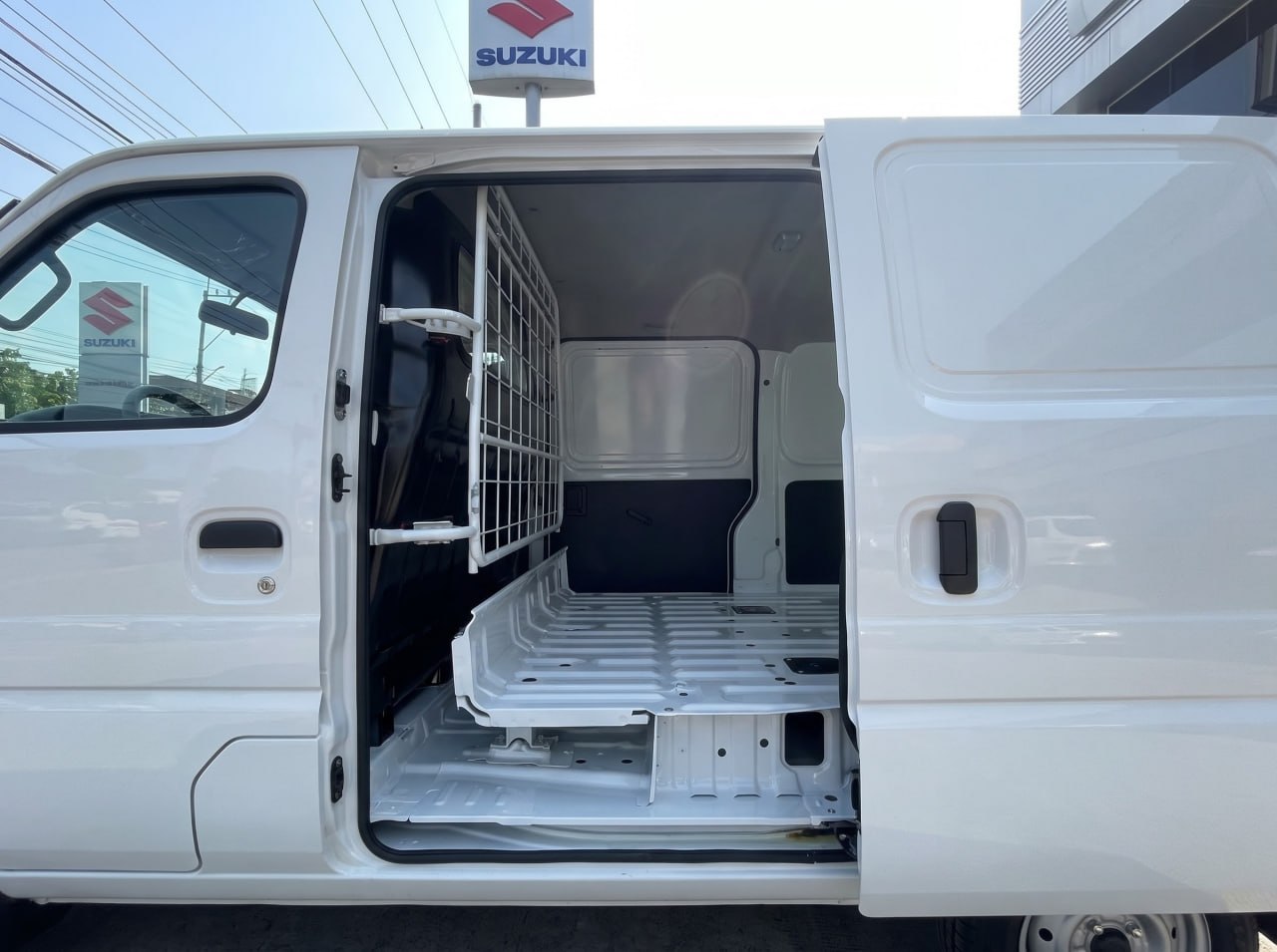 Ảnh ngoại thất và nội thất xe Suzuki Eeco màu trắng, góc chụp từ bên hông khi mở cửa lùa bên phụ, hiển thị khoang chở hàng và vách ngăn lưới thép.