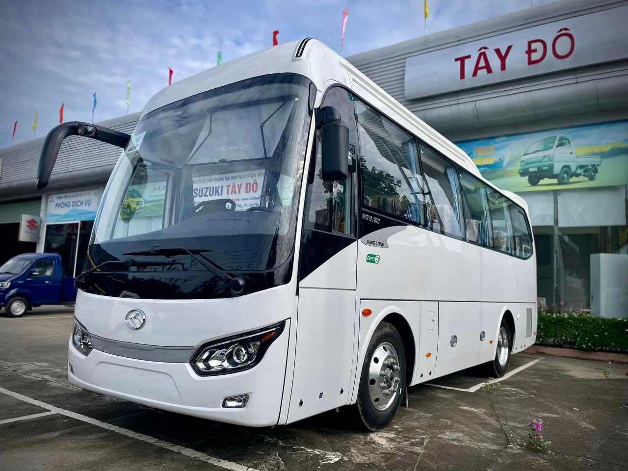Ảnh chụp ngoại thất xe khách King Long Nova Slim màu trắng từ góc xéo phía trước bên trái, đỗ trước showroom Ô Tô Tây Đô
